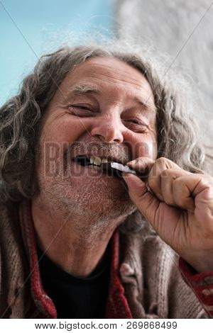 Happy Senior Man With Missing Teeth Smiling As He Bites In To A Piece Of Chocolate.