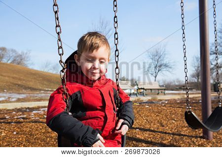 Boy Sitting On A Swing In The Park In Spring. The Child Swinging Alone On The School Yard. Copy Spac