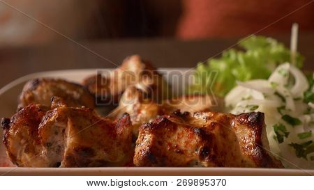 Close Of Roasted Meat Lying On A White Plate With Greens On A Table