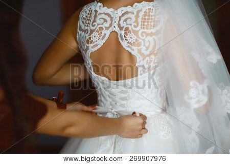 Bridesmaid Preparing Bride For The Wedding Day. Bridesmaid Helps Fasten A Wedding Dress The Bride Be