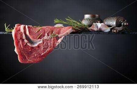Raw Beef Steak With Peppermill, Garlic And Rosemary. Black Background, Copy Space.
