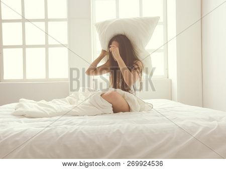 Young caucasian woman covering her head and ears with pillows.