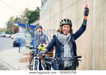 Active Senior Couple With Electrobikes Standing Outdoors On A Road In Town.