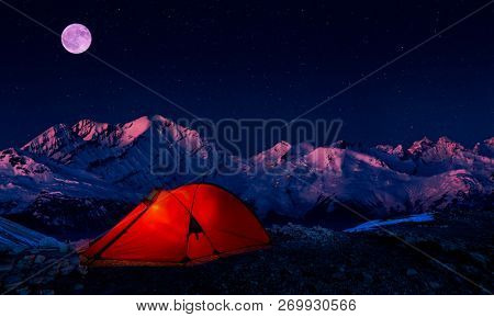 Night bivouac in Mountains, milion star hotel under night sky, red illuminated tent on pass in Alps.