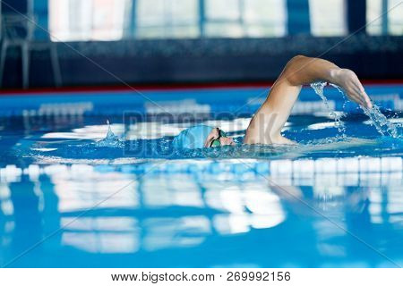 Image of young athlete in blue cap swimming in pool