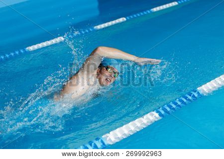 Photo of sportsman in blue cap swimming in style of crawl in swimming pool