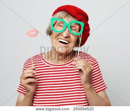 lifestyle, people and party concept: funny grandmother wearing red clothes holding falce glasses and  ready for party