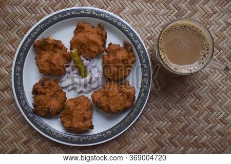 Top View Of Dal Vada, Masala Vada, Chana Vada Served With Cut Onion And Green Chilly And Tea On Serv