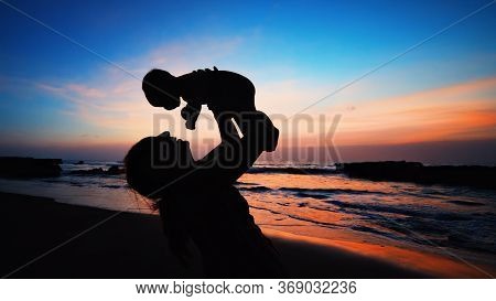 Happy Family Black Silhouette On Sunset Sky Background. Young Mother, Baby Son Have Fun Together, Wa