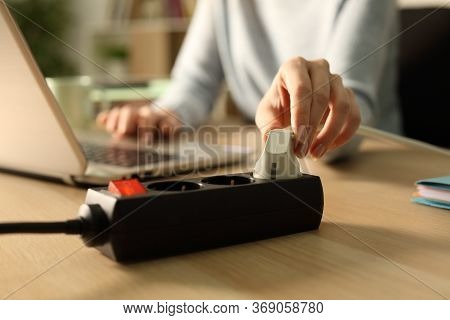 Close Up Of Woman Hand Plugging Plug On A Power Strip Socket At Night Using Laptop On A Desk At Home
