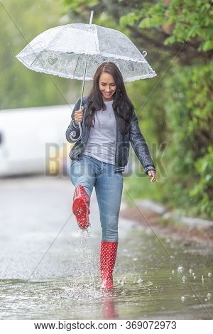 Woman With An Umbrella Walking In Rainboots In A Puddle Under A Heavy Rain.