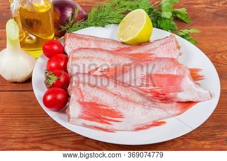 Raw Headless Gutted Carcasses Of Redfish Also Known As Ocean Perch On The Dish With Lemon And Cherry