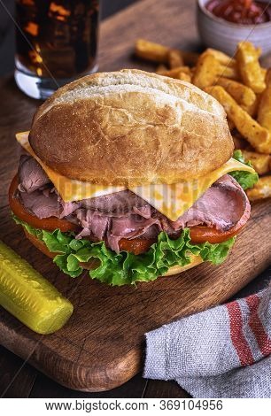 Roast Beef Sandwich With Cheese, Tomato And Lettuce On A Bun On A Wooden Cutting Board