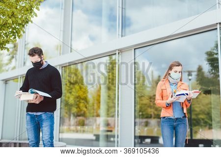 Students learning on campus keeping social distance, in the background the main building