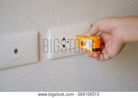 Hand Holding Electric Tester For Checking Plug At The Power Outlet In On The Wall. Check The Quality
