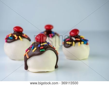 Banana Split Cake Balls With White Coating And Chocolate Drizzled On Along With Sprinkles And A Cher
