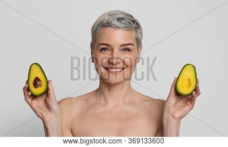 Anti-aging Foods. Beautiful Nude Mature Woman Holding Two Avocado Halves And Smiling At Camera, Stan