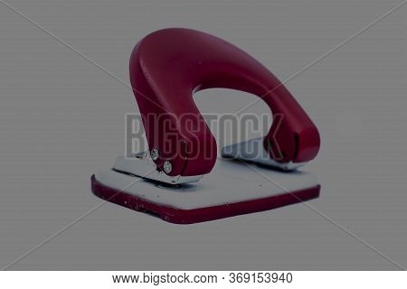 Red-colored Hole Puncher/ Paper Puncher Isolated On A Grey Colored Corporate Background.