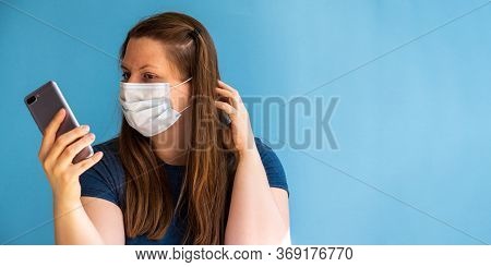 European Girl Blogger In Medical Mask On The Blue Background With Mobile Phone In Your Hand. Phone W