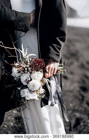 Destination Iceland Wedding. Close-up Of The Brides Bouquet, The Groom Hugs The Bride By The Waist.