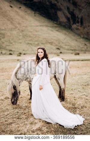 Destination Iceland Wedding Photo Session With Icelandic Horses. The Bride Walks Across The Field, N