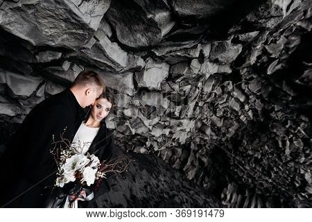 Destination Iceland Wedding. Wedding Couple Under A Rock Of Basalt Stones. Bride And Groom On The Bl