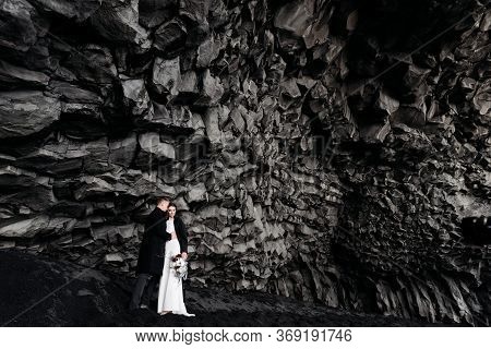 Destination Iceland Wedding. Wedding Couple Under A Rock Of Basalt Stones. Bride And Groom On The Bl