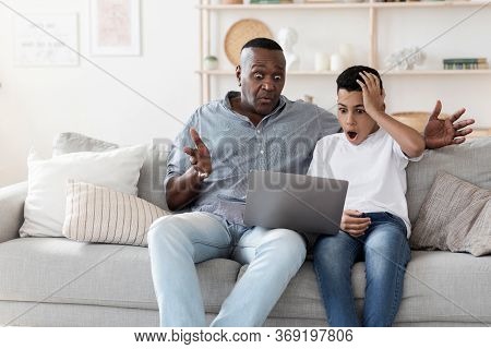 Shocked Black Grandad And His Preteen Grandson Watching Scary Movie On Laptop, Sitting At Home With 