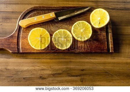Some slices of lemon cut on a wooden board next to a knife on a rustic background