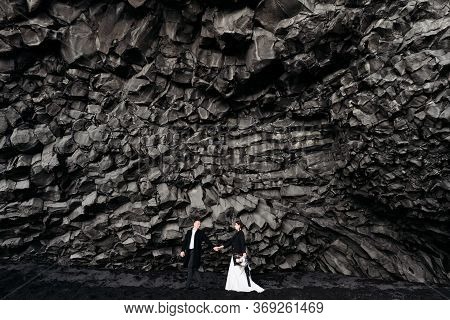 Destination Iceland Wedding. Wedding Couple Under A Rock Of Basalt Stones. Bride And Groom On The Bl
