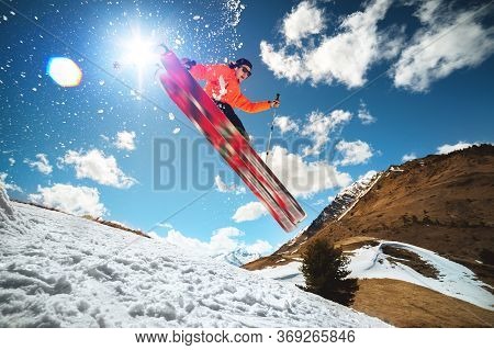 A Young Stylish Man In Sunglasses And A Cap Performs A Trick In Jumping With A Kicker Of Snow Agains