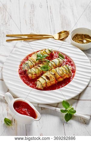 Ricotta And Spinach Stuffed Zucchini Rolls Baked In Tomato Sauce, Served On A Plate With A Fresh Bas