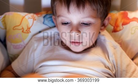 Closeup Image Of Little Boy Lying In Bed At Night And Looking On Glowing Smartphone Or Tablet Screee