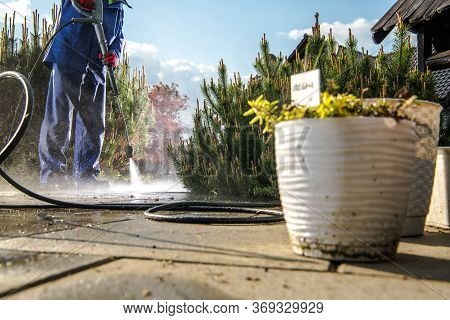 Men Wearing Wet Coat Cleaning Backyard Garden Paths Using Pressure Washer. Home And Garden Maintenac