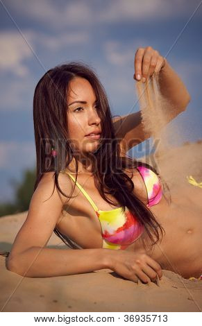 En smuk pige i en bikini hælder sand