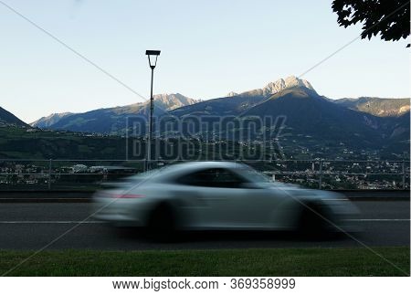 A Blurred Car In Merano, Alto Adige, Italy. Personal Transportation Concept. Peak Ifinger In The Bac