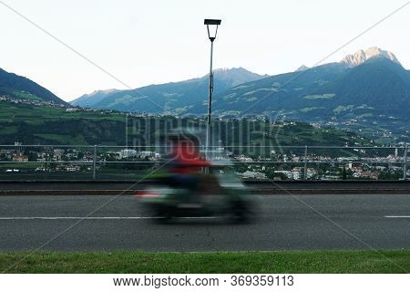 A Man On A Scooter, Blurred, In Merano, Alto Adige, Italy. Personal Transportation Concept. Peak Ifi