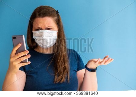 European Girl Blogger In Medical Mask On The Blue Background With Mobile Phone In Your Hand. Phone W