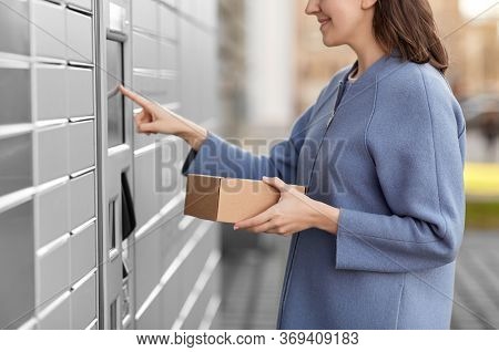 mail delivery and post service concept - close up of happy smiling woman with box at outdoor automated parcel machine choosing operation on touch screen