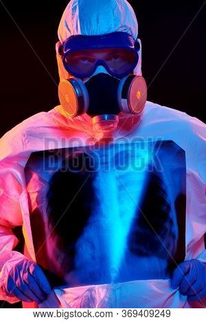 COVID-19 or 2019-nCoV. Portrait of a doctor in a protective PPE suit showing an x-ray picture of the lungs of a patient with coronavirus pneumonia. 