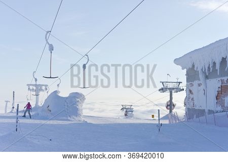 A Single Skier Heads Down A Run Having Disembarked From Ski Lifts That Rise Up Above The Clouds Into