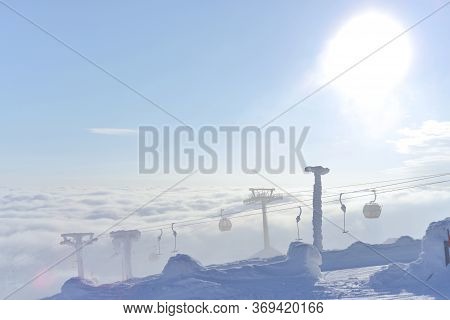 The Sun Flares From Behind These Gondola And T-bar Ski Lifts As They Rise, Frozen In Snow And Ice, F