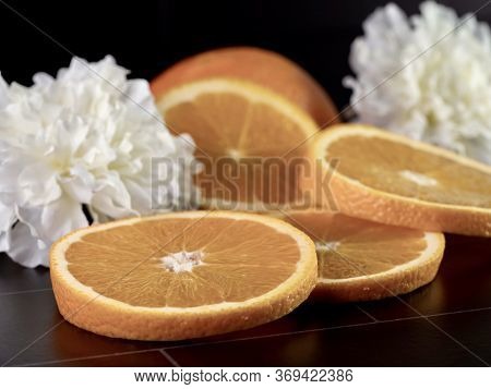 Fresh Orange Slices And A Half Orange Laying On A Black Tile Counter With Two White Carnations For D