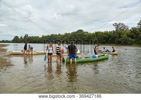 DOMBRAD, HUNGARY - CIRCA 2017: Group of young people preparing for a nomad canoe trip on the river Tisza with canoes ashore. The second larges river of Hungary, popular for water activities.