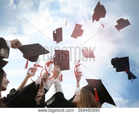 Happy Students With Diplomas Throwing Graduation Hats In Air Outdoors