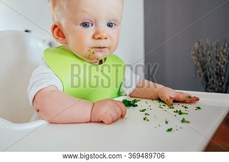 Portrait Of Cute Baby Girl Sitting Messy After Feeding. Little Child Chewing At Dining Table. Led We