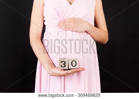 Cropped Portrait Of Pregnant Woman In Pink Dress Holding Cubes Which Show Thirty Weeks Of Pregnancy 