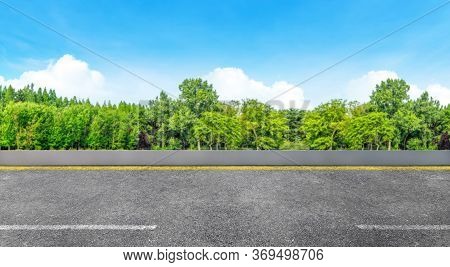 Side View Of Asphalt Straight Street Roadway Of Lanes With Lines And Green Trees With Blue Sky In Ba
