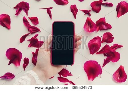 Woman Holds Smartphone In Hand On Peony Petals Floral Background. Flat Lay