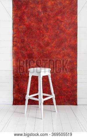 White High Wooden Stool With A Red Textured Background. Bar Chair In White Wooden Minimalist Room. S